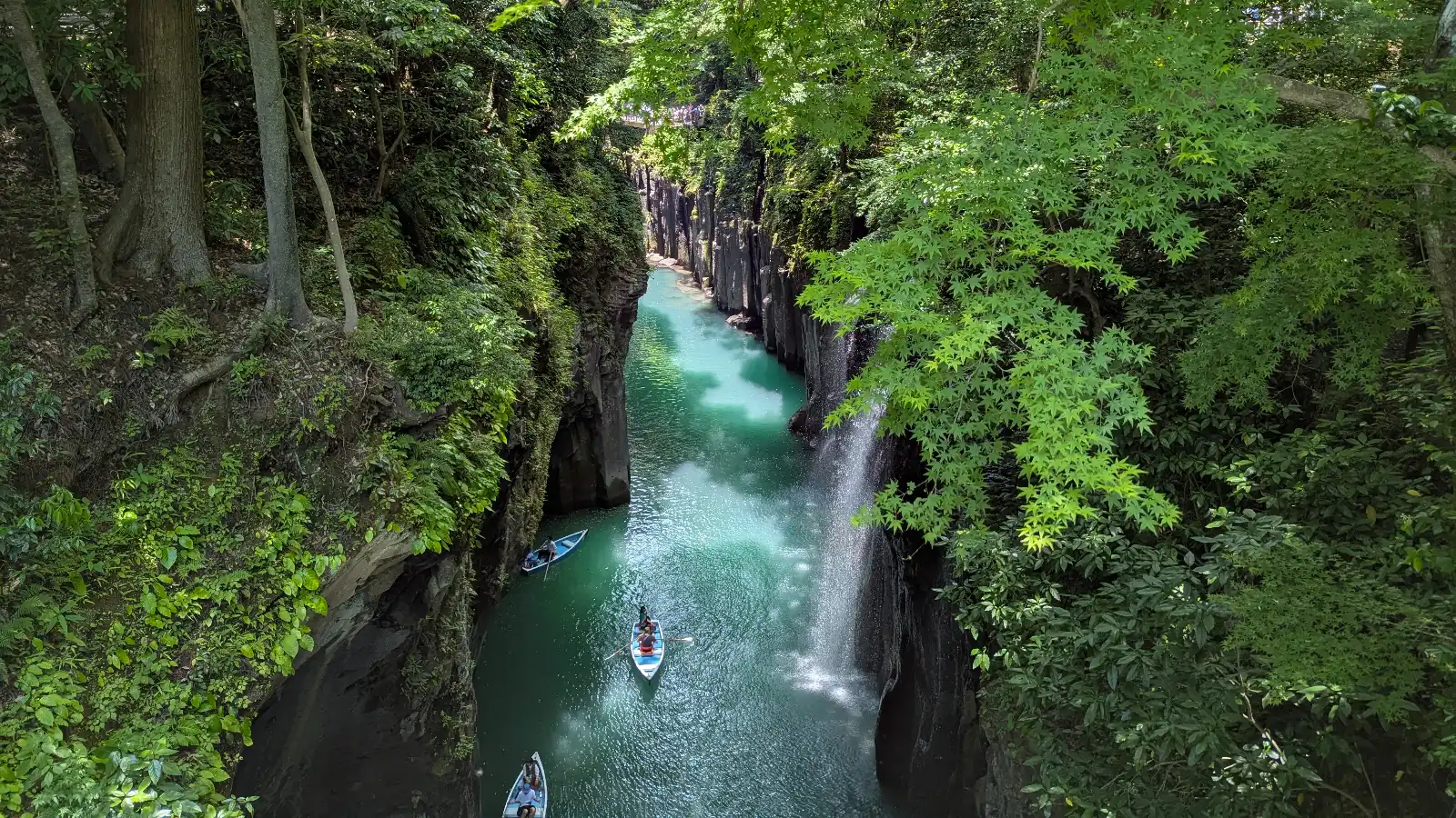 Families explore Takachiho Gorge in Miyazaki, Japan, paddling through emerald waters surrounded by towering cliffs and lush greenery. A family-friendly adventure in Kyushu highlighting the scenic boat ride experience at Takachiho Gorge.