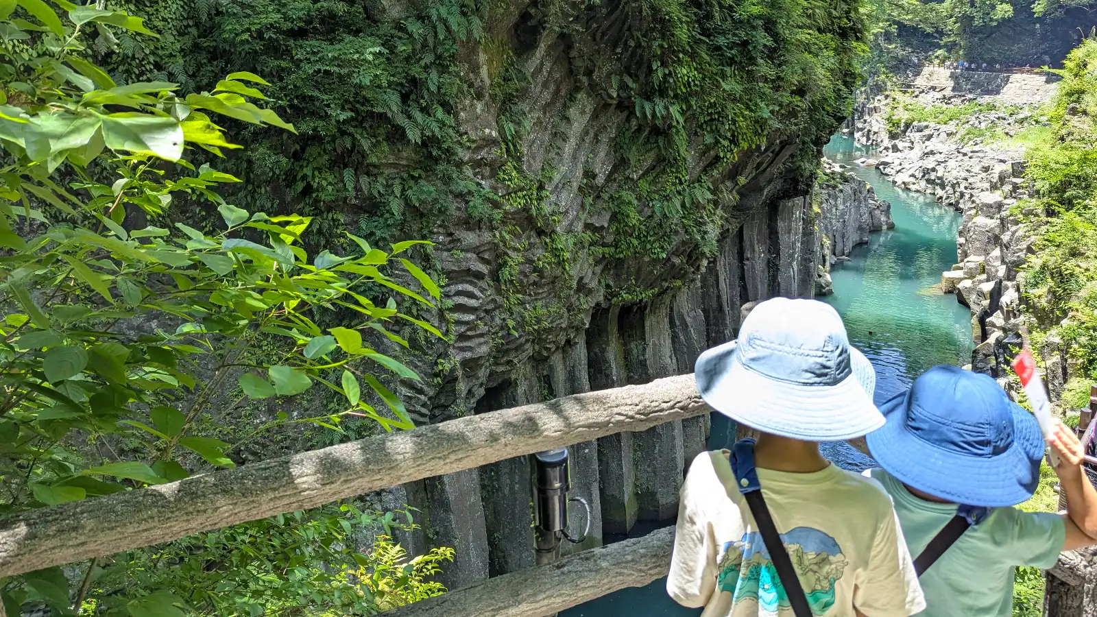 Luca and Nico looking out over Takachiho Gorge in Miyazaki, Kyushu Japan, with lush cliffs and emerald water below.