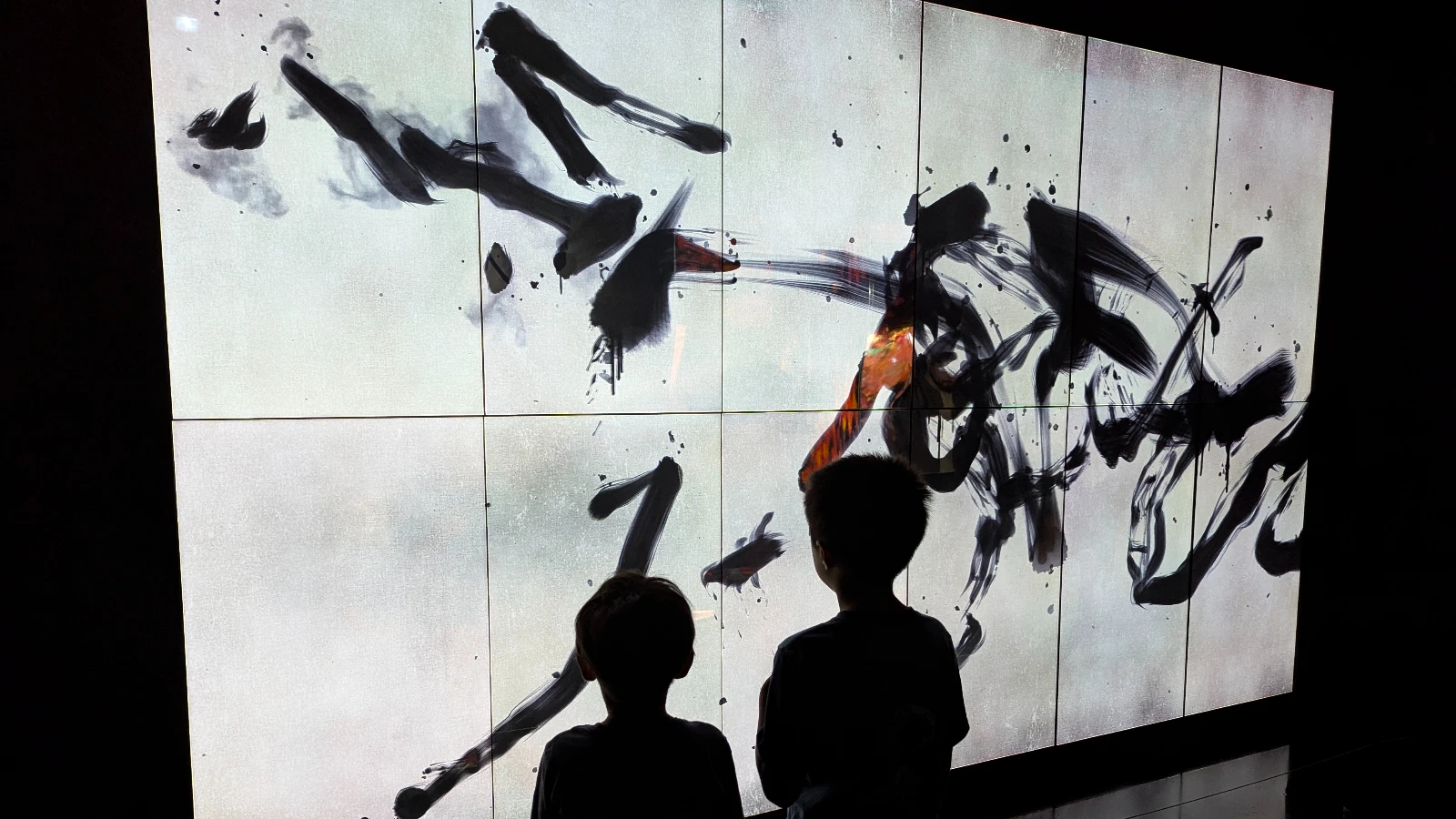 Children watching a dynamic calligraphy-style digital artwork projection at teamLab Borderless Tokyo.