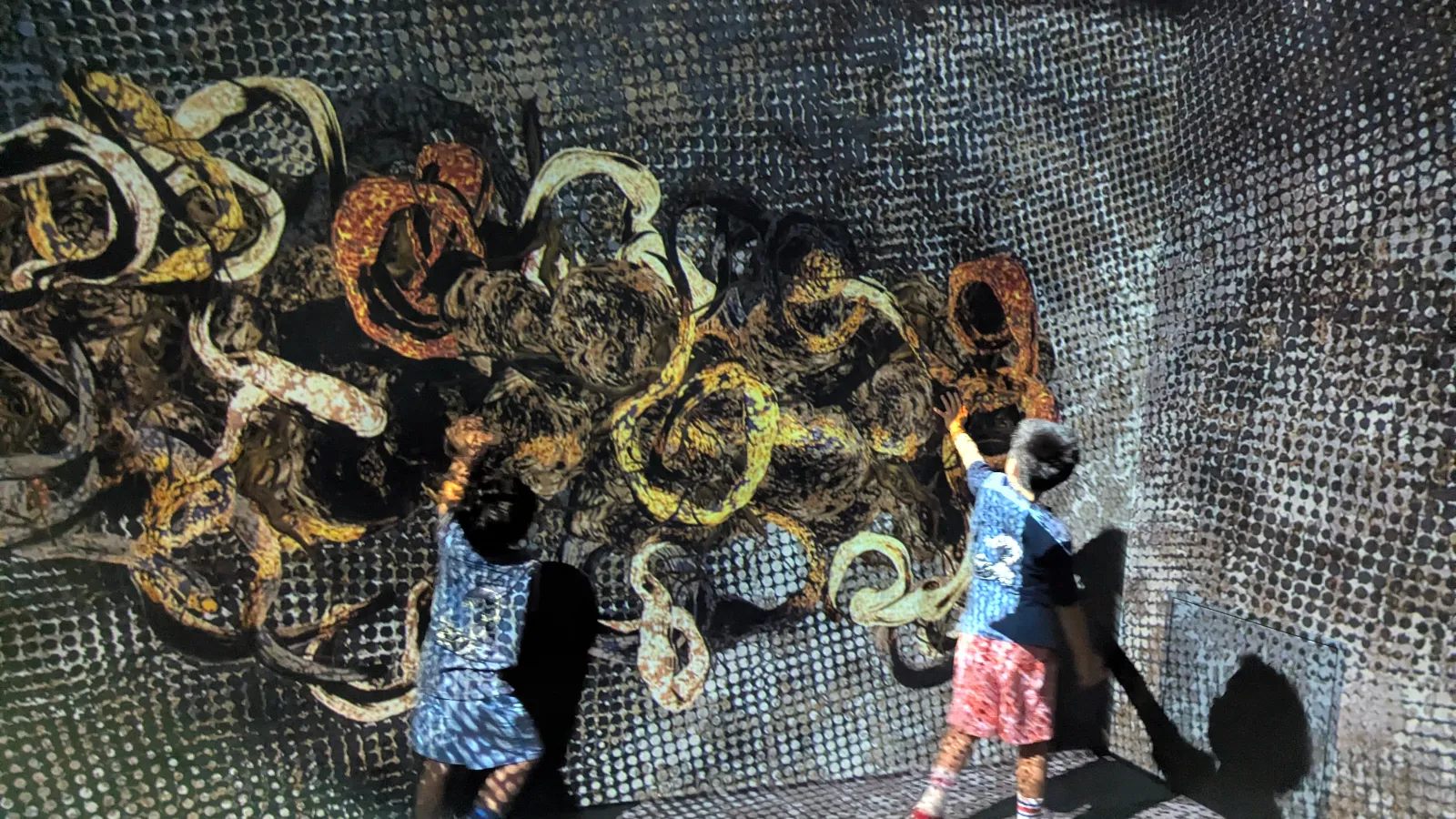Kids interacting with an abstract moving projection at teamLab Borderless, touching the textured digital artwork on the wall.