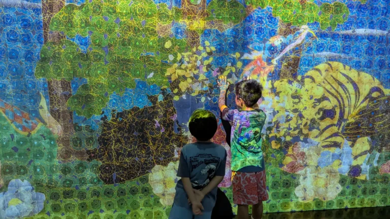 Children exploring a bright nature-themed digital projection at teamLab Borderless Tokyo, filled with colorful plants and animals.