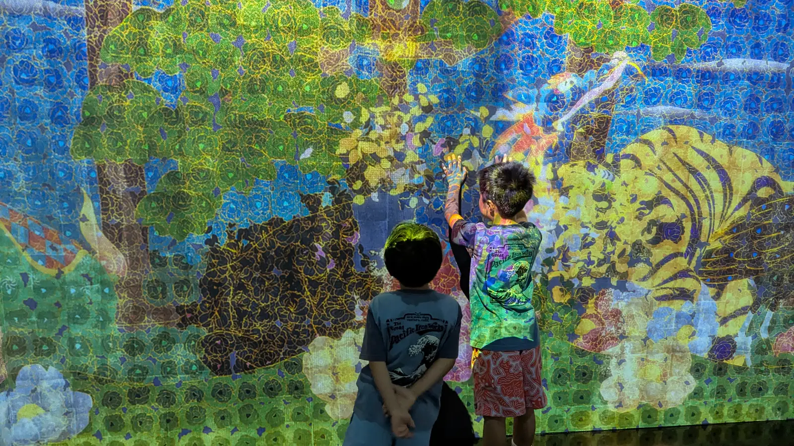 Children exploring a bright nature-themed digital projection at teamLab Borderless Tokyo, filled with colorful plants and animals.