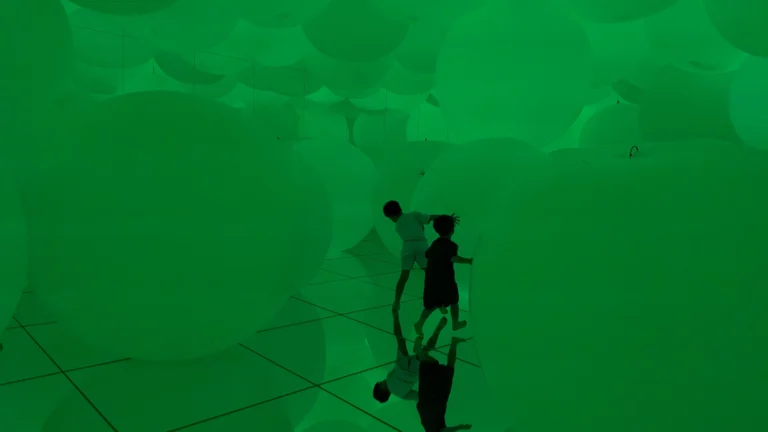 Kids walking through the Floating Balloon Room at teamLab Planets Tokyo, surrounded by giant glowing spheres in a mirrored space.