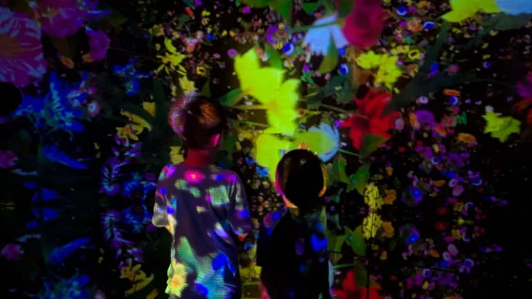Children watching colorful digital flower projections move across the walls and floor inside teamLab Planets Tokyo.