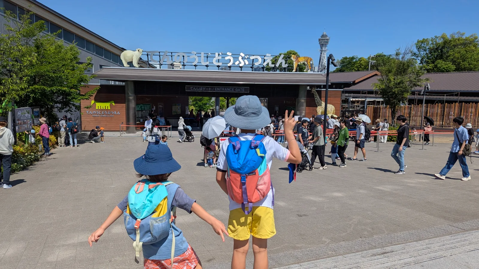 Luca and Nico at the Tenshiba Gate entrance to Tennoji Zoo in Osaka, with Tsutenkaku tower behind.
