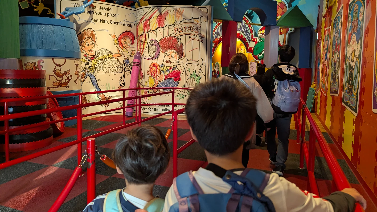Kids standing in the colorful Toy Story-themed attraction queue at Tokyo DisneySea, surrounded by giant illustrated pages, crayons, and bright carnival decorations.