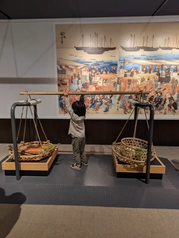 Luca lifting traditional Edo-period goods at the Edo-Tokyo Museum in Tokyo, learning about Japanese history through interactive exhibits.