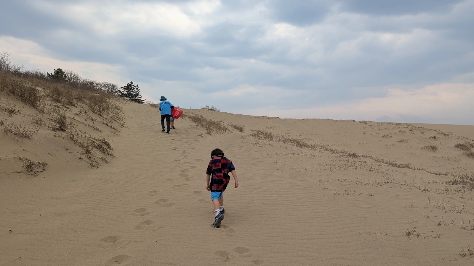 Family climbing the Tottori Sand Dunes with a sled, a fun family travel activity in Japan.
