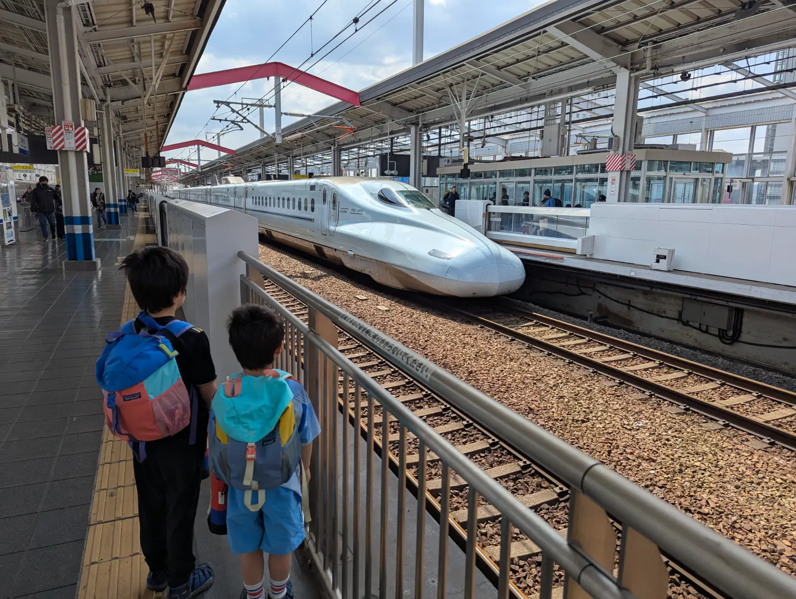 Luca and Nico watching a Shinkansen arrive at the station, capturing the excitement of train travel in Japan with kids