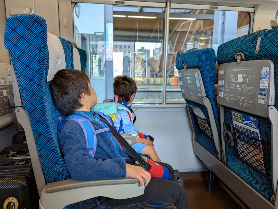 Luca and Nico relaxing in reserved seats on a Shinkansen train, highlighting the comfort of train travel in Japan with kids