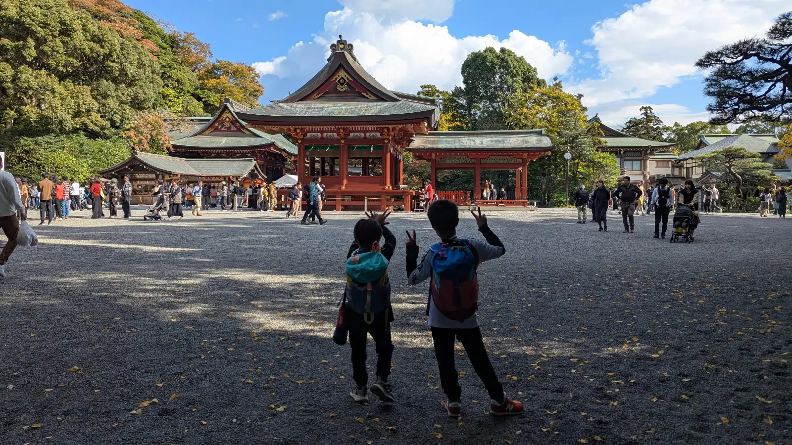 Children standing in the courtyard of Tsurugaoka Hachimangu Shrine in Kamakura, facing the historic shrine buildings with visitors nearby.
