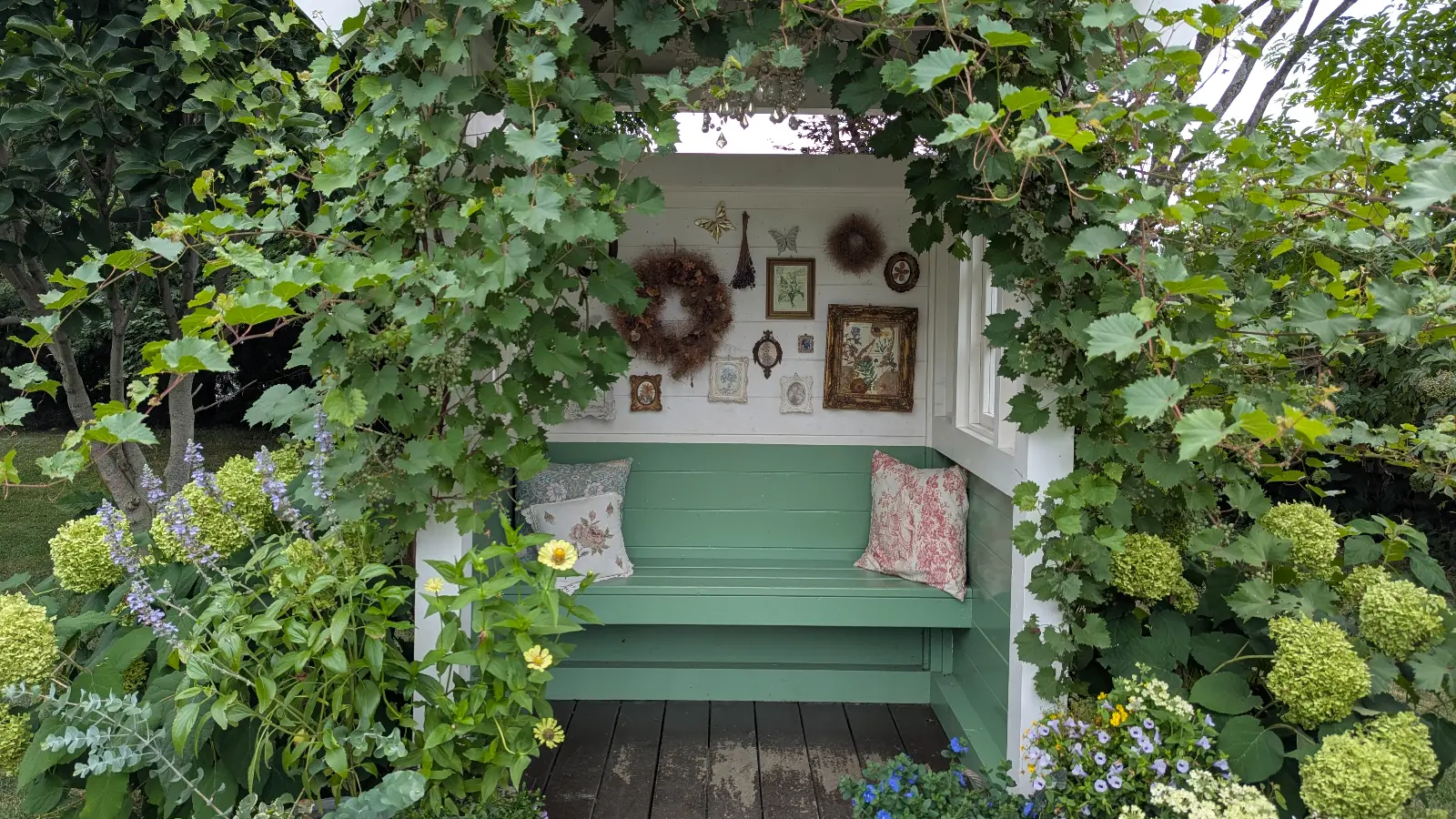 A cozy green garden bench surrounded by vines, flowers, and framed art at Ueno Farm Gnomes Garden in Asahikawa, Hokkaido.