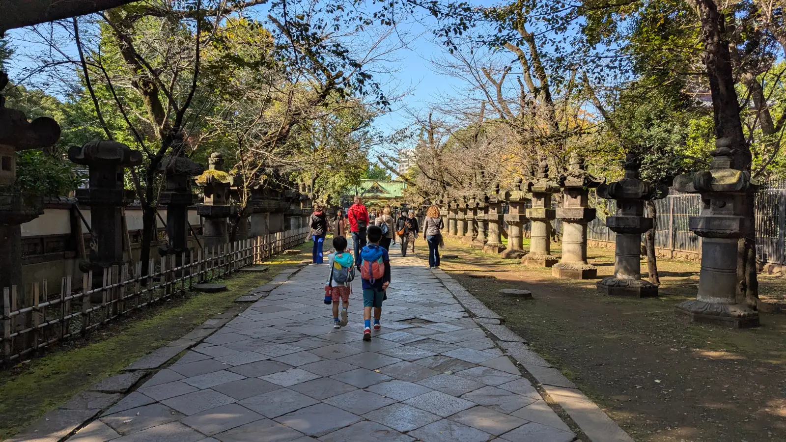 Luca and Nico walking along a quiet stone path lined with lanterns near a shrine in Ueno, showing the calm and family-friendly atmosphere of the neighborhood