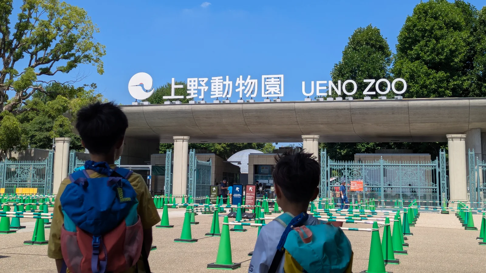 Luca and Nico standing at the entrance of Ueno Zoo (上野動物園) in Tokyo, Japan, looking toward the zoological gardens gate.