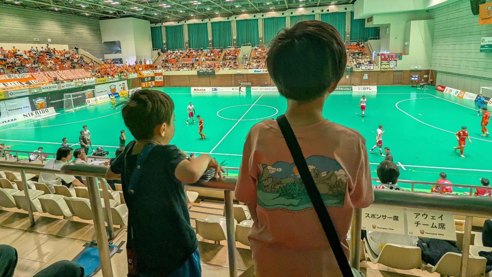Luca and Nico watch a VASAGEY Oita futsal match, a lively, family-friendly sports experience during Japan travel with live action and cheering fans.