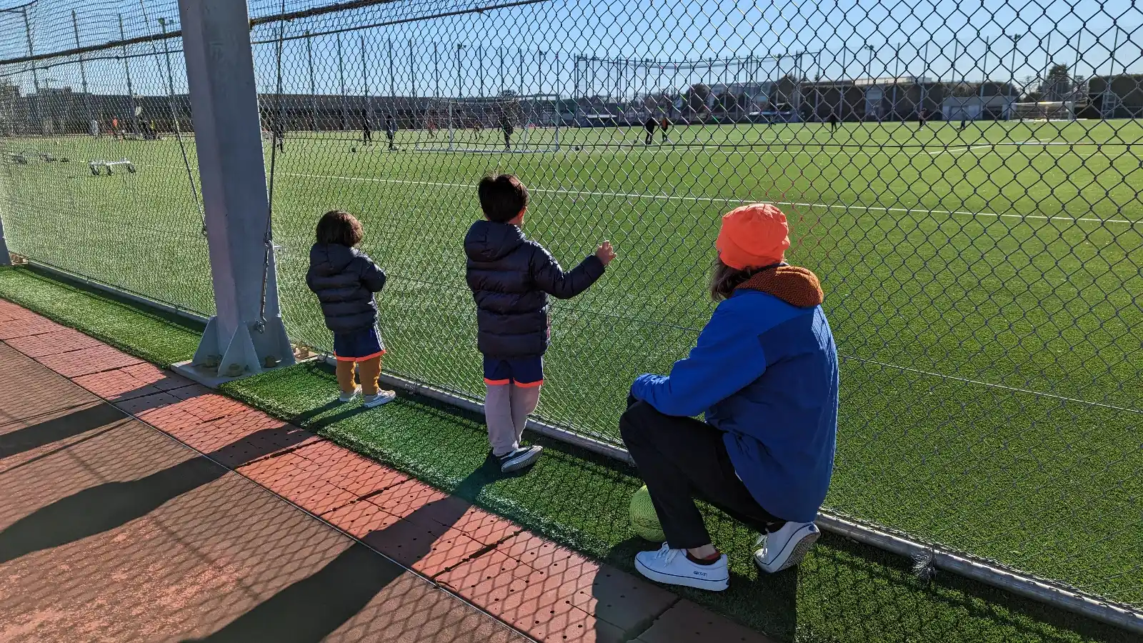 Children bundled in winter jackets watching a soccer practice in Japan, showing everyday family life and outdoor activities during winter with kids.