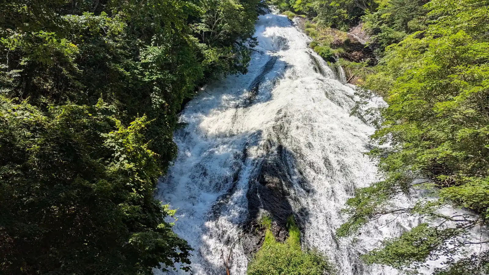 Wide view of Yudaki Cascades (湯滝) in Nikko, Japan, showing the powerful waterfall surrounded by lush green forest.